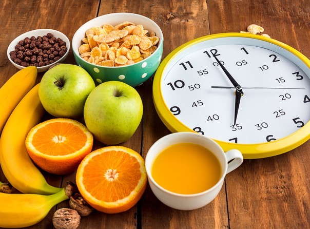 składniki dietetycznego śniadania do pracy: płatki, owoce, orzechy i sok; obok żółty zegar