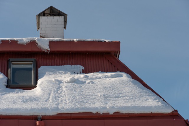 The roofs of the buildings are covered with snow and ice after a big snowfall. Huge icicles hang from the facades of buildings. The fall of icicles carries a danger to people's lives.