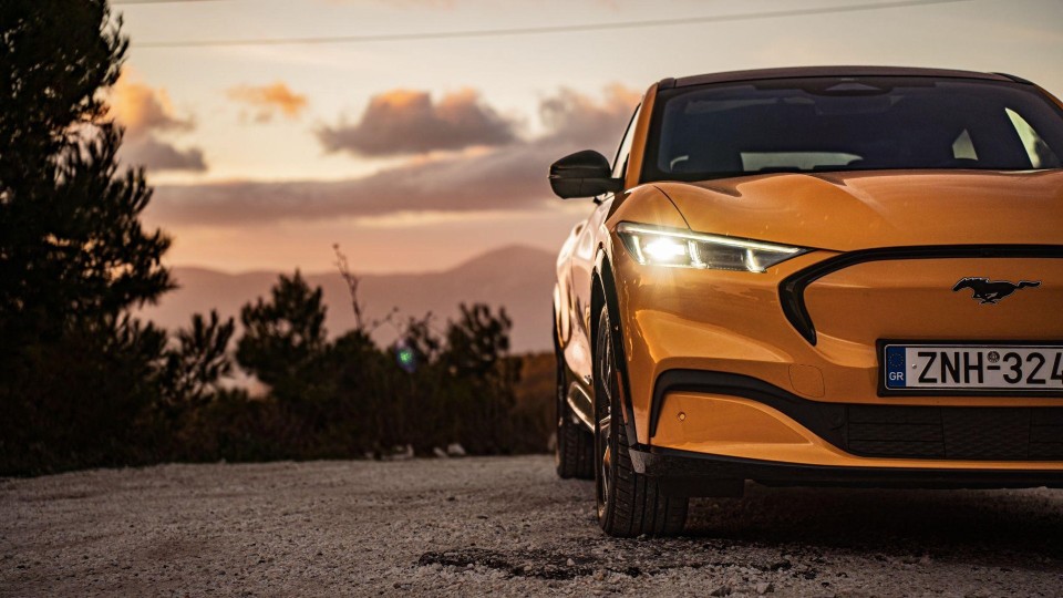 Żółty samochód stoi na poboczu jezdni. To elektryczny Ford Mustang Mach-E, który wyróżnia się nowoczesnym designem.